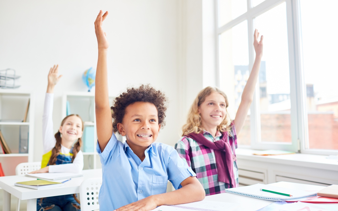 Дети школьники с поднятой  рукой в классе на 1 сентября 