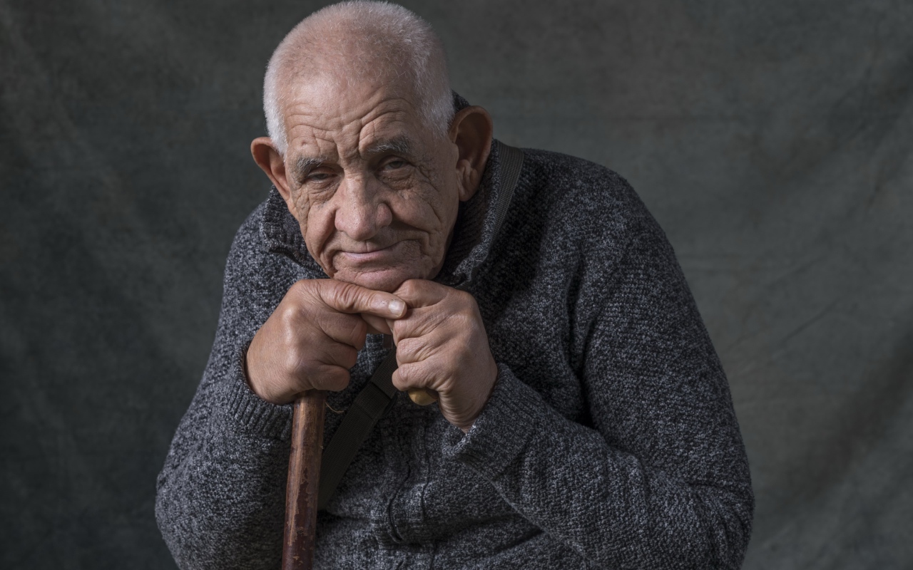 Пожилой мужчина в теплом свитере на сером фоне 