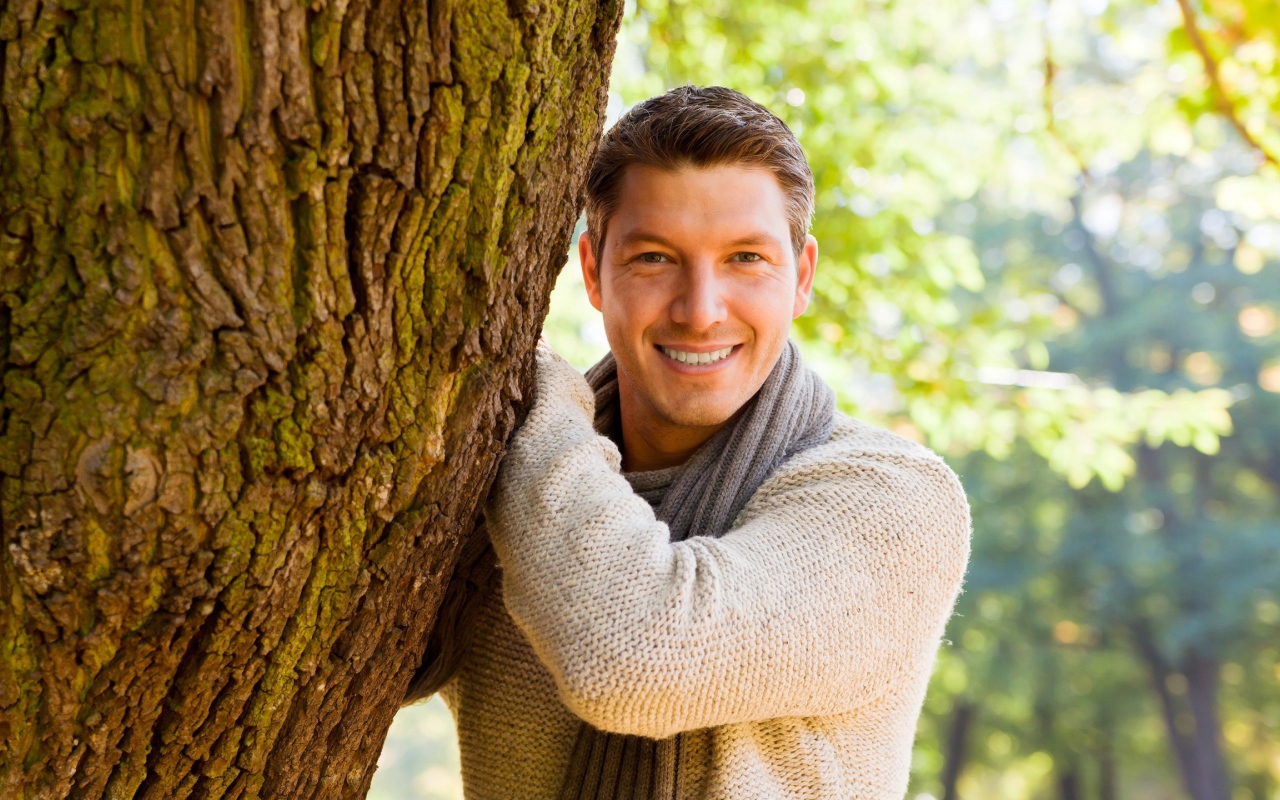 Улыбающийся мужчина стоит у дерева 