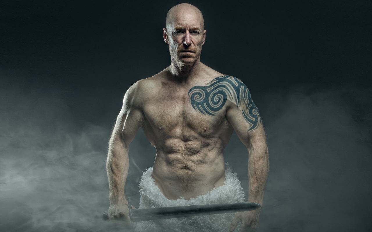 Сильный мужчина с мечом с татуировками на теле 