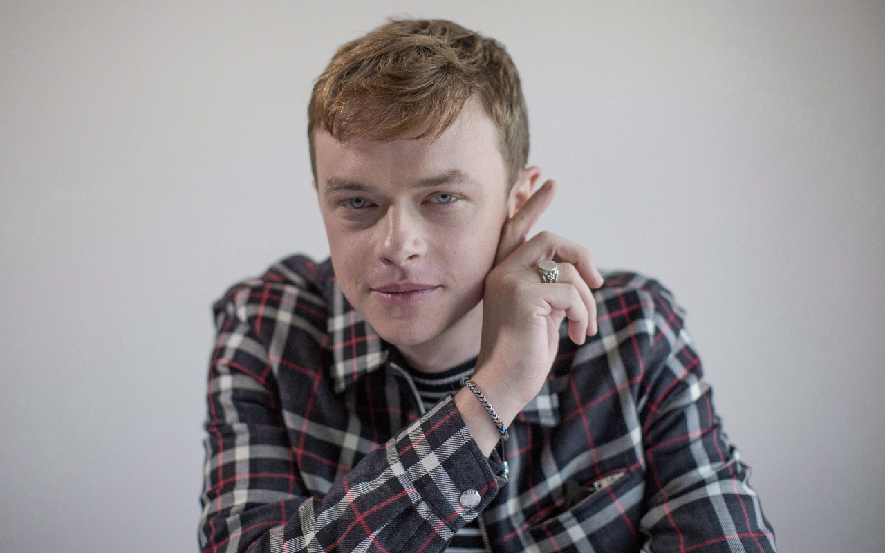 Молодой актер Дэйн Дехаан в рубашке на сером фоне