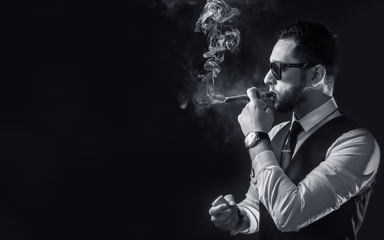 Мужчина с сигарой в руке на черном фоне 