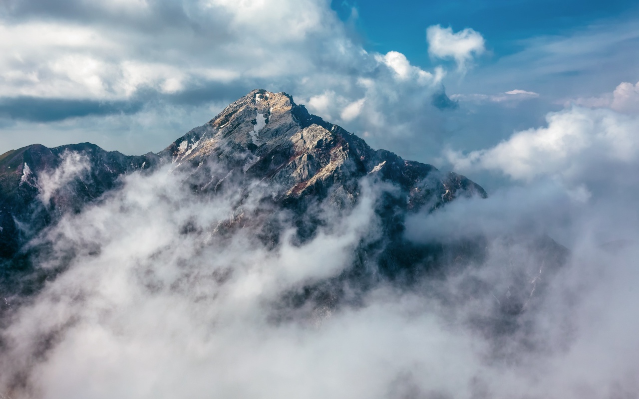 Большая высокая гора в густых белых облаках
