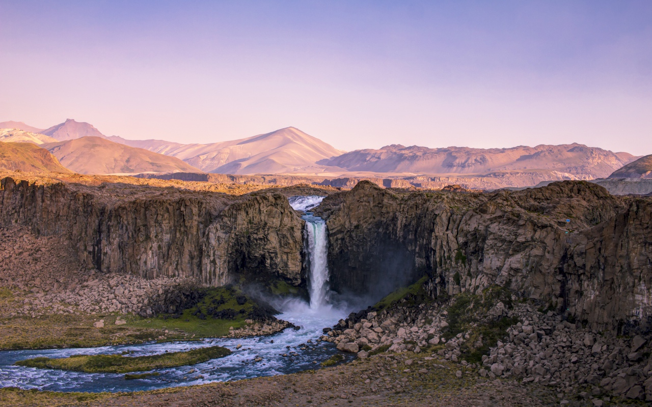Водопад стекает по каменному склону горы на рассвете 