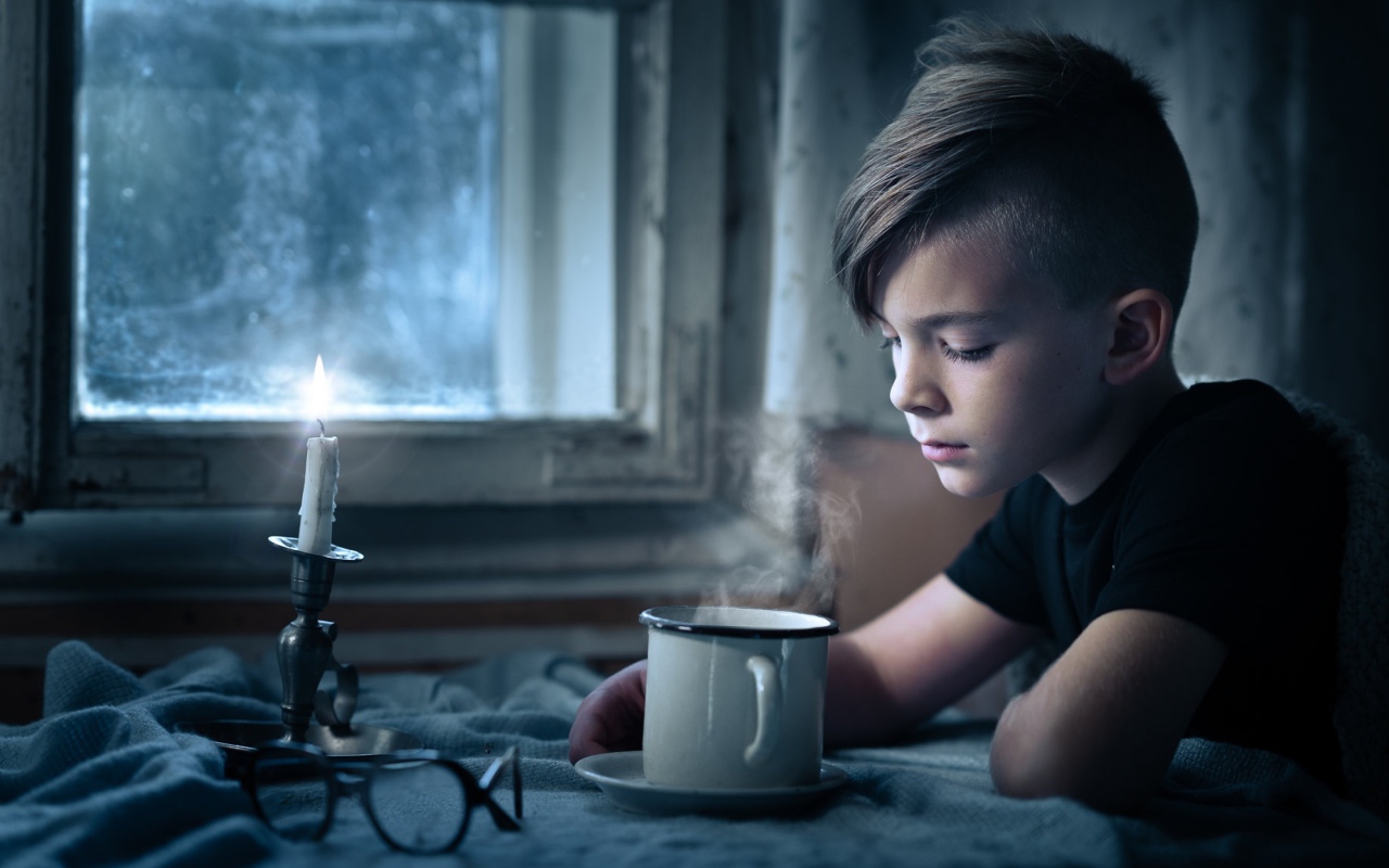 Маленький мальчик сидит за столом при свете свечи 