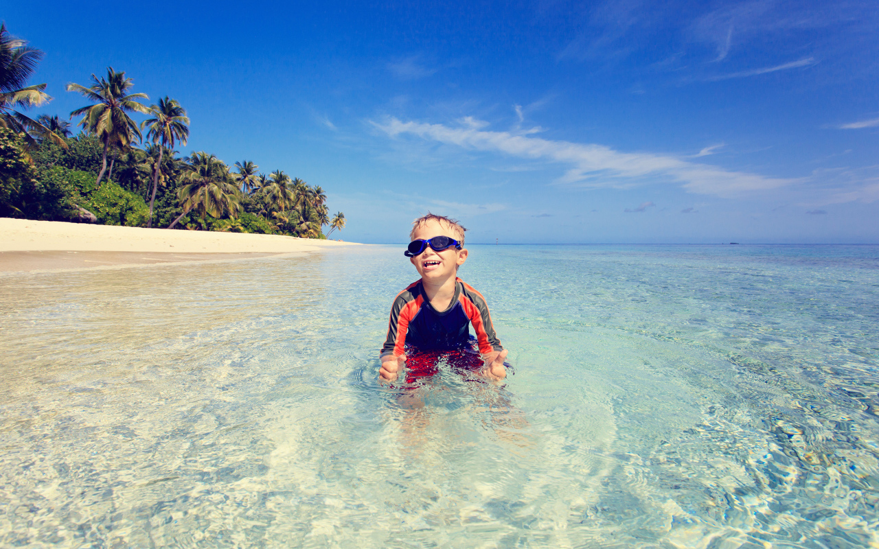 Мальчик в очках сидит в воде на пляже 