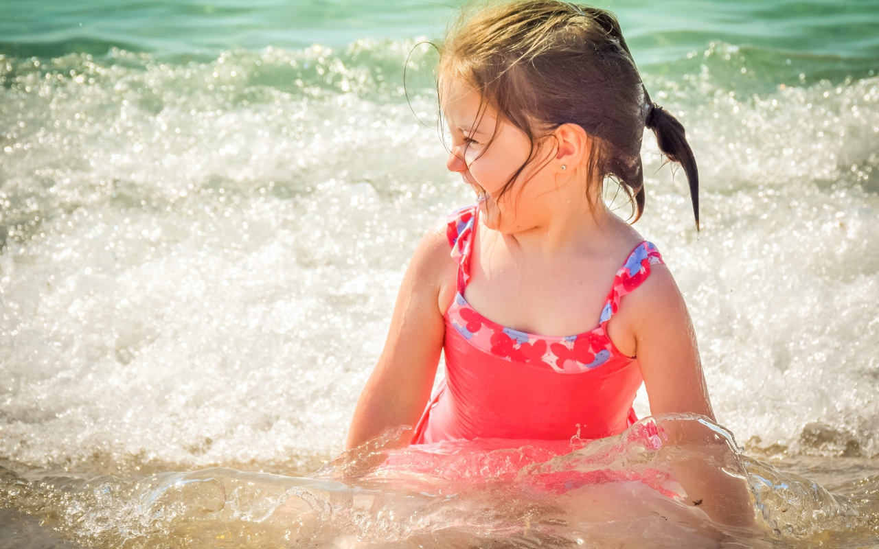 Веселая маленькая девочка в купальнике сидит в воде 