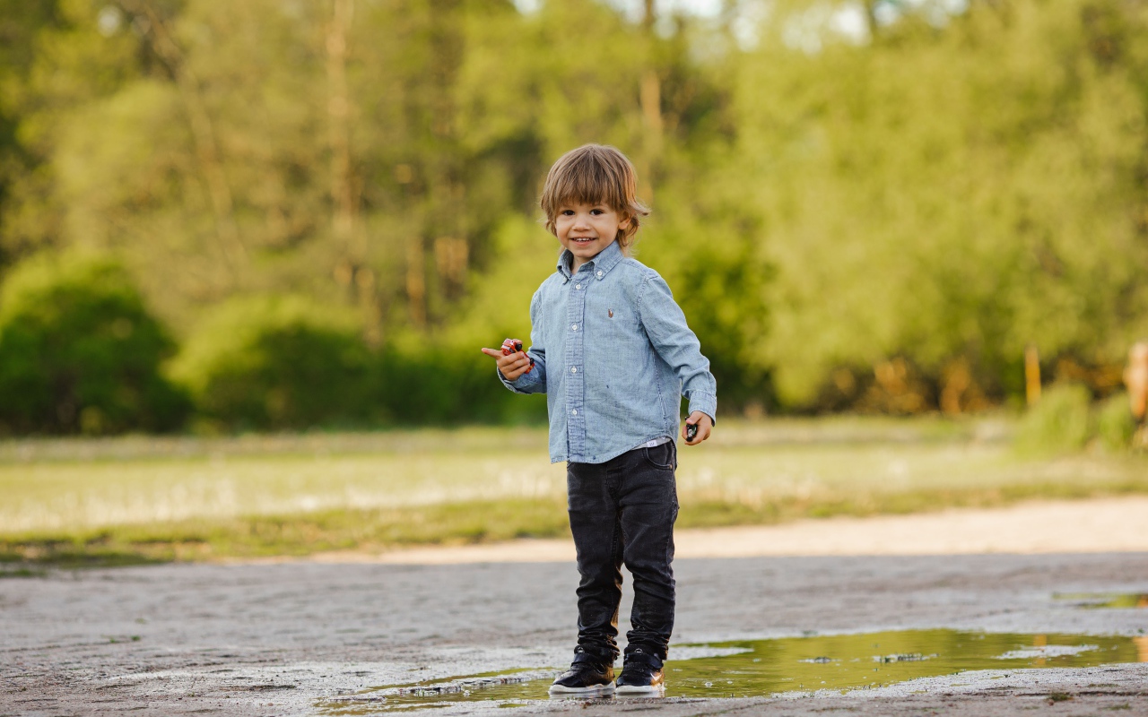 Маленький мальчик стоит в луже на дороге 