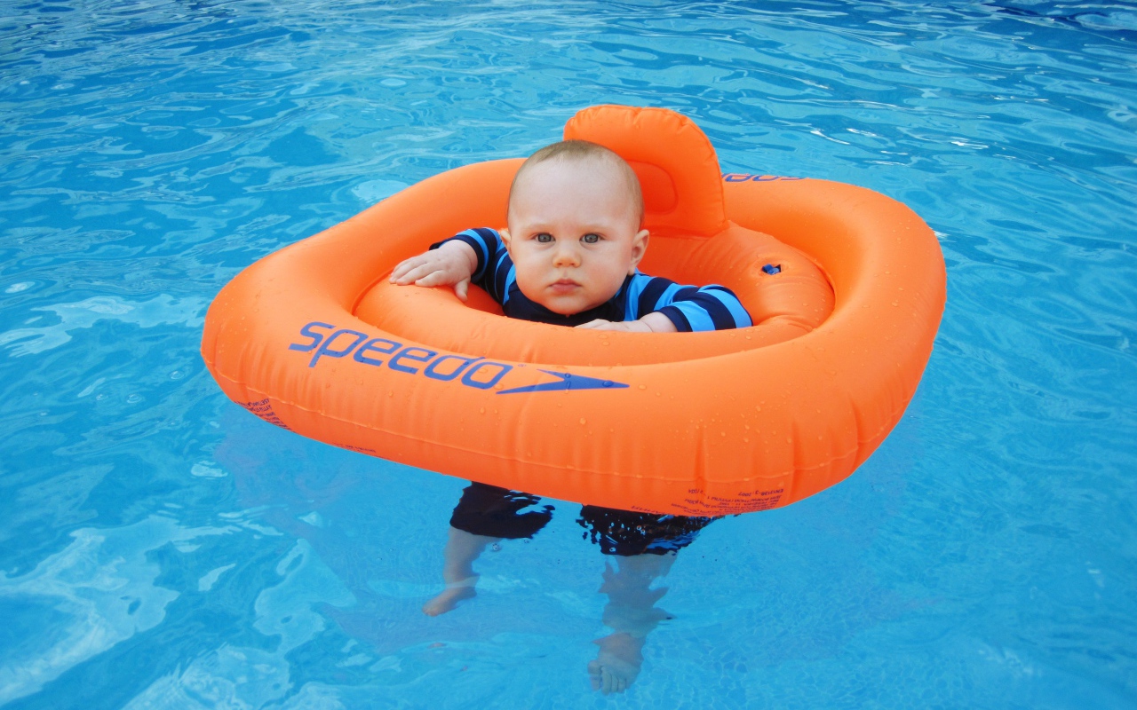 Маленький ребенок с оранжевым спасательным кругом в бассейне