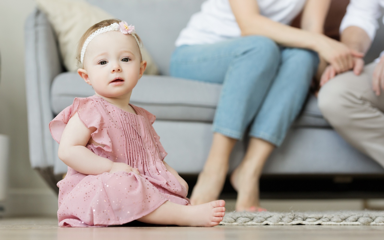 Маленькая девочка в розовом платье сидит на полу