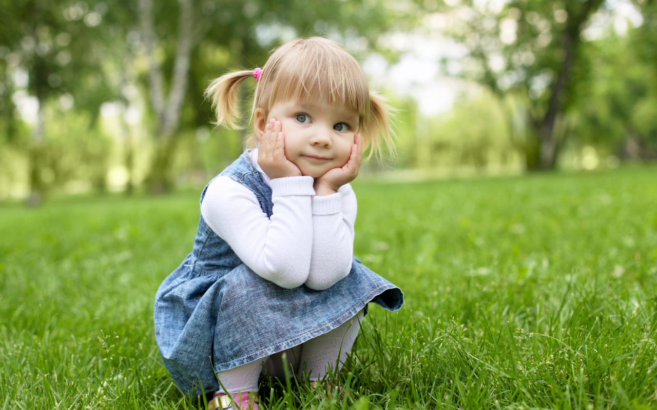 Маленькая девочка в сарафане сидит на траве 