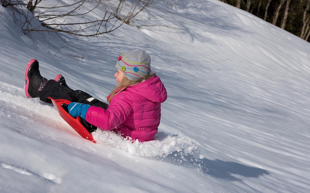 Маленькая девочка катится с заснеженной горки 