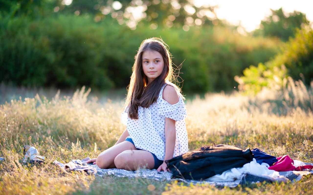 Маленькая девочка сидит на покрывале на земле 