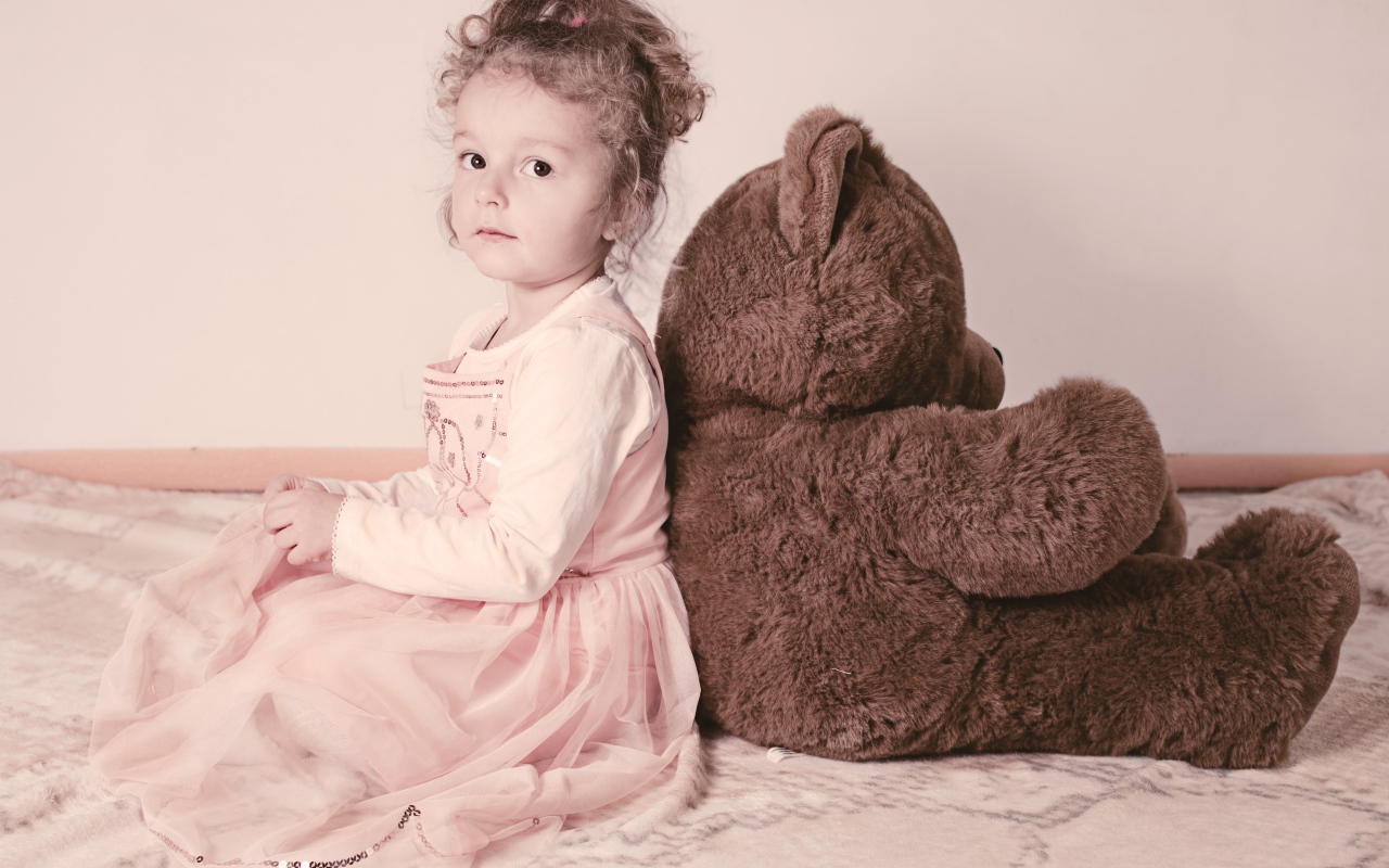 Маленькая девочка сидит с большим медведем