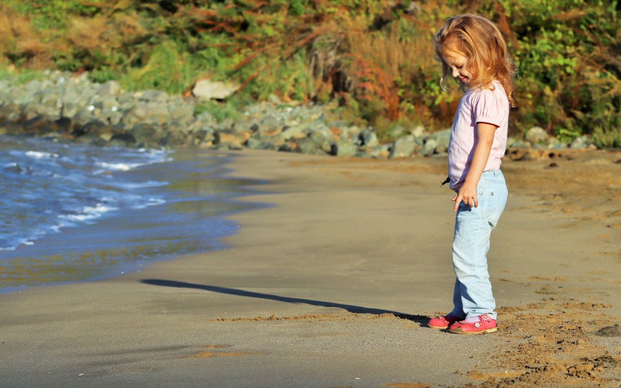 Маленькая девочка гуляет по мокрому песку 