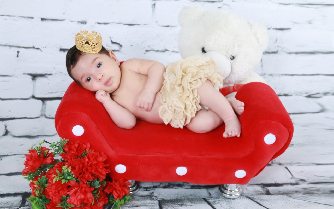 Маленькая принцесса лежит на красном диване у стены 