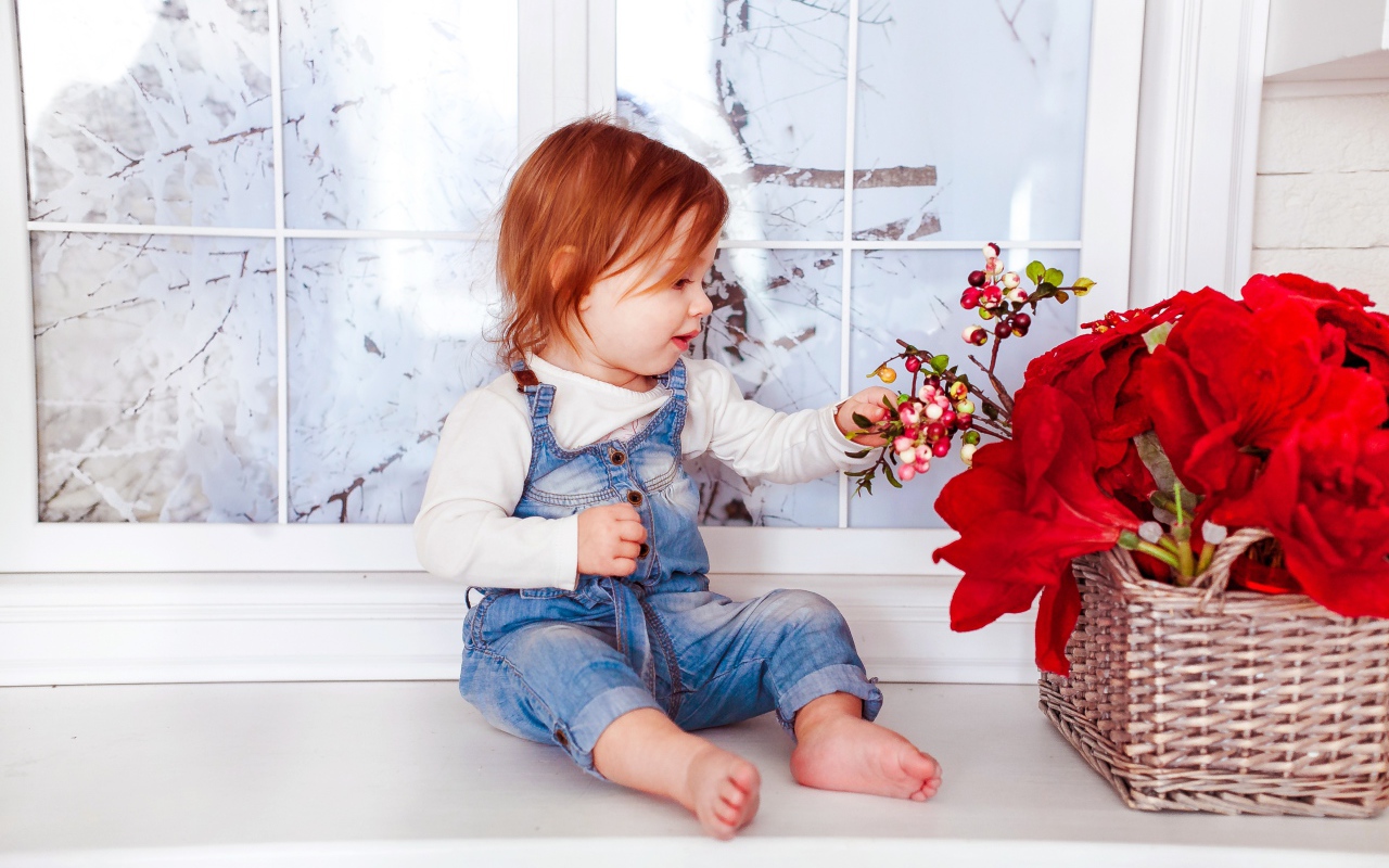 Маленькая рыжеволосая девочка сидит у корзины цветов 