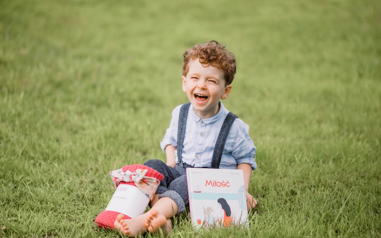 Маленький улыбающийся мальчик сидит на зеленой траве с книгой 