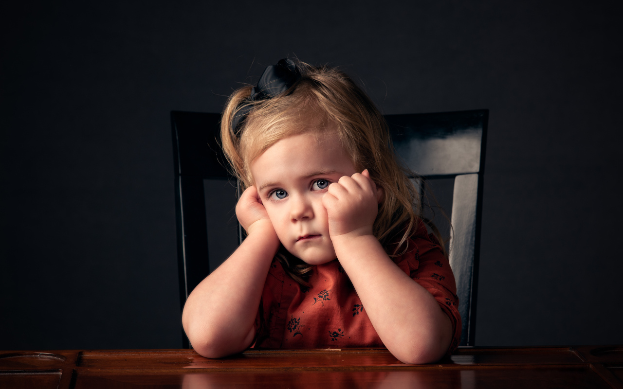 Грустная маленькая девочка сидит за столом