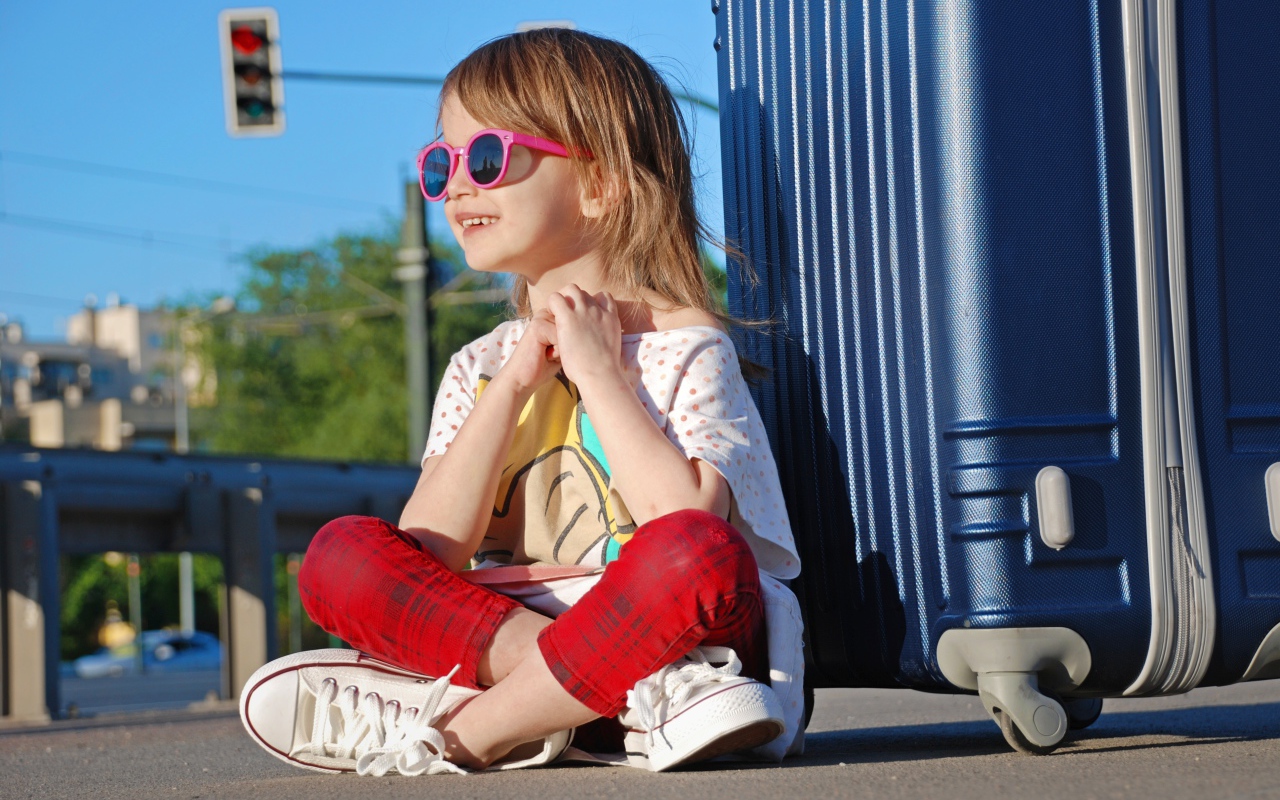 Улыбающаяся маленькая девочка в очках с чемоданом