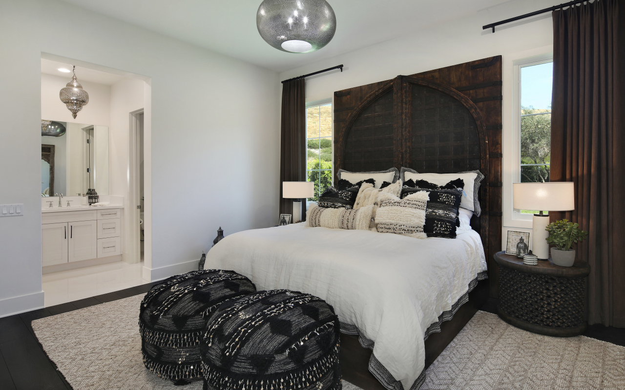 Большая кровать в спальне с большими окнами со шторами