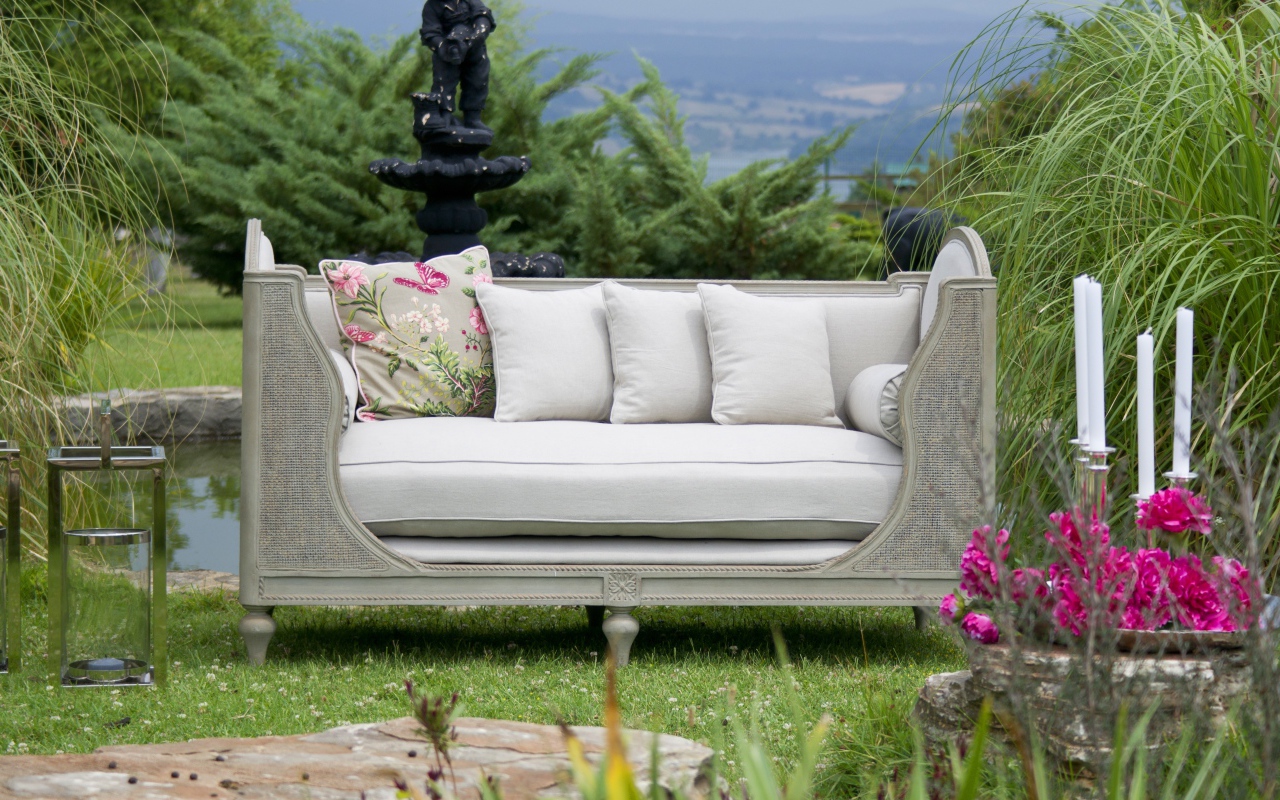Большой серый диван в саду у пруда 