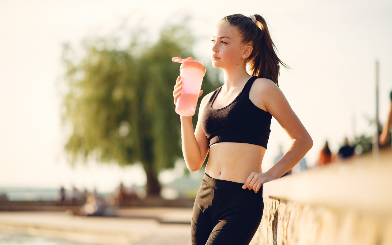 Спортивная девушка в черном пьет воду