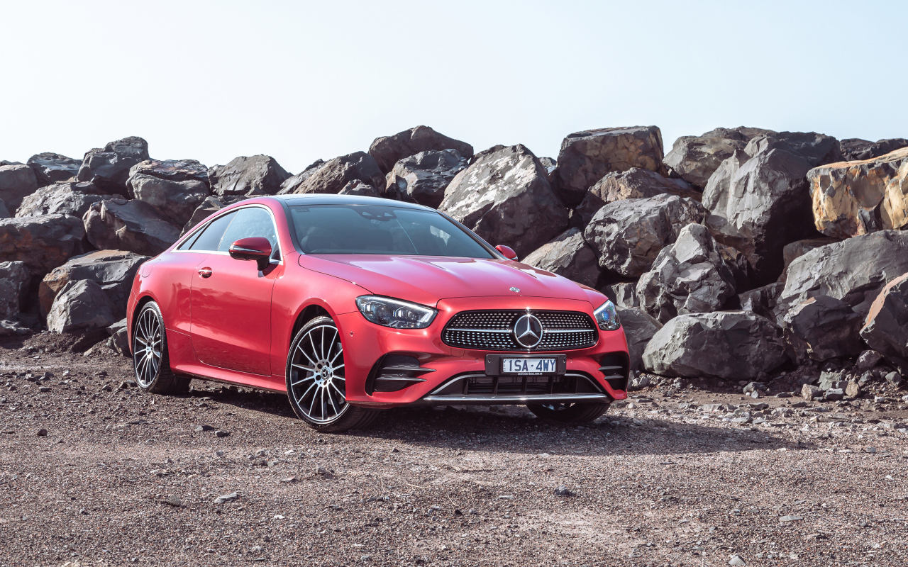 Красный автомобиль Mercedes-Benz E 350 AMG Line Coupé 2023 года у камней