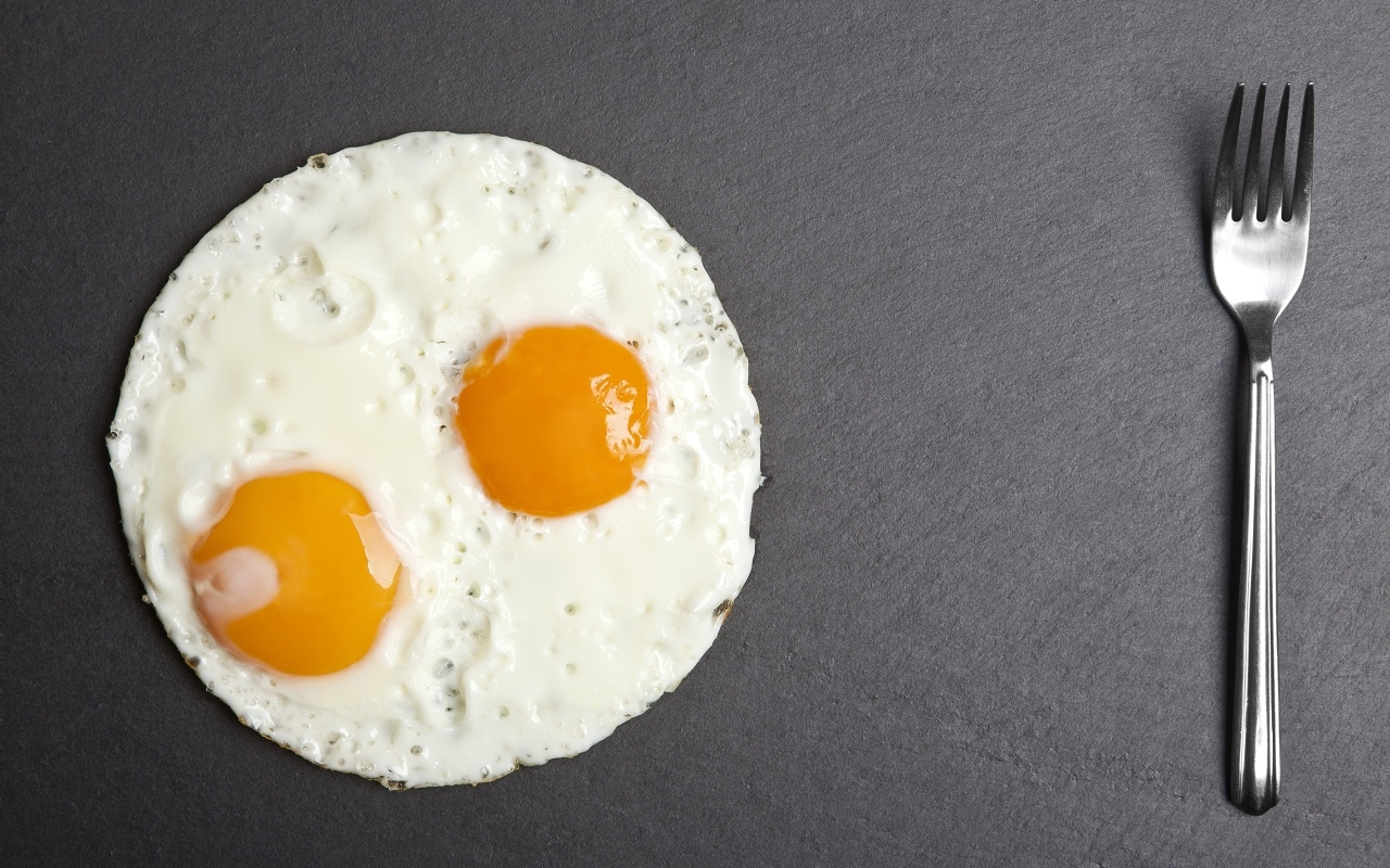 Яичница глазунья с вилкой на сером столе