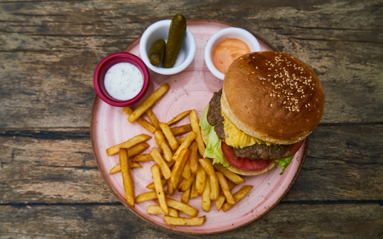 Гамбургер на тарелке с картофелем фри, огурцами и соусом