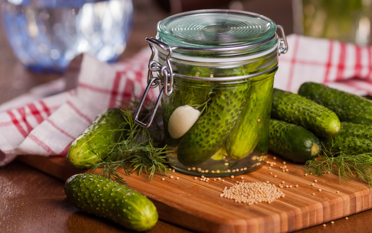 Маринованные огурцы в банке на столе со свежими