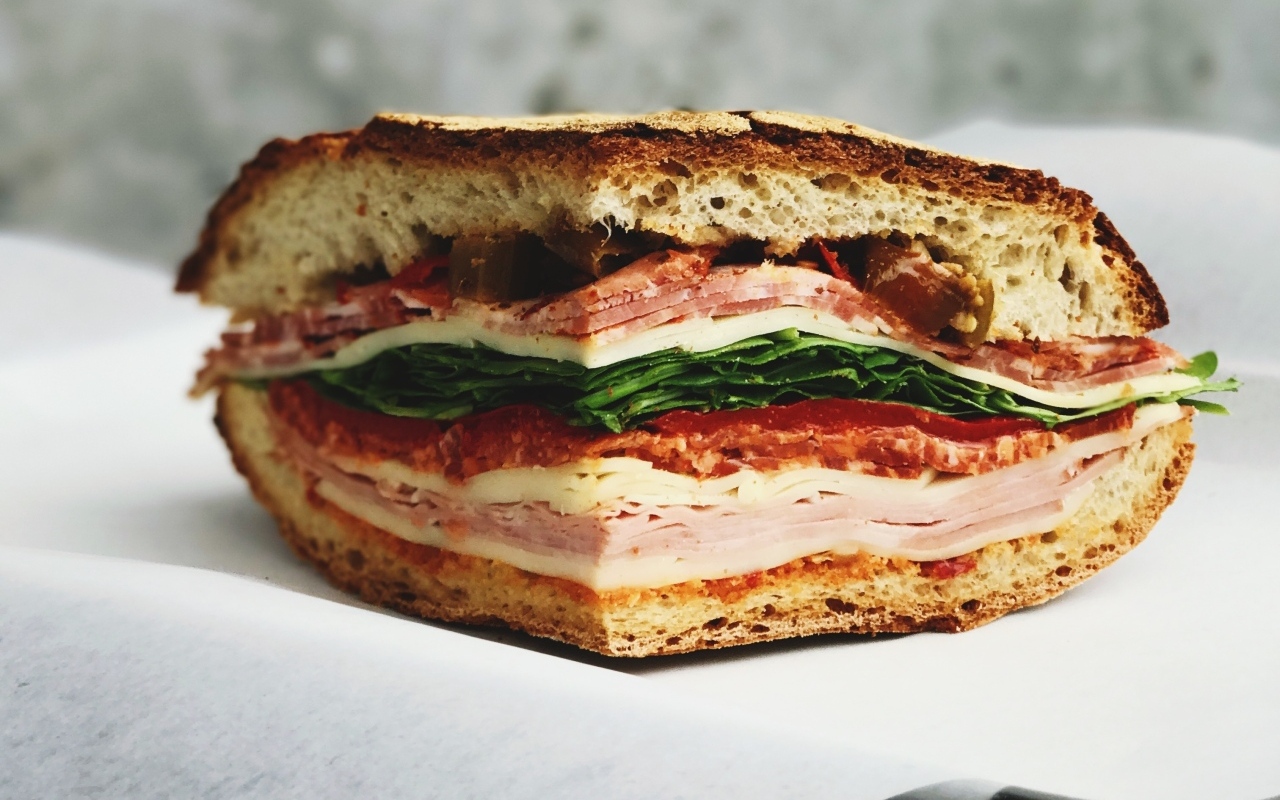 Кусок булки с колбасой, ветчиной и листьями салата