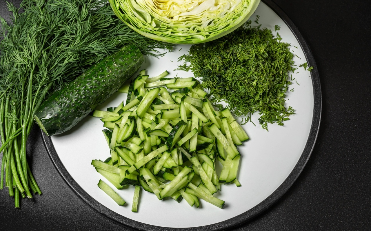 Нарезанные огурцы на столе с капустой и укропом