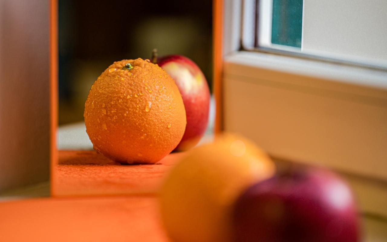 Апельсин и яблоко отражаются в зеркале