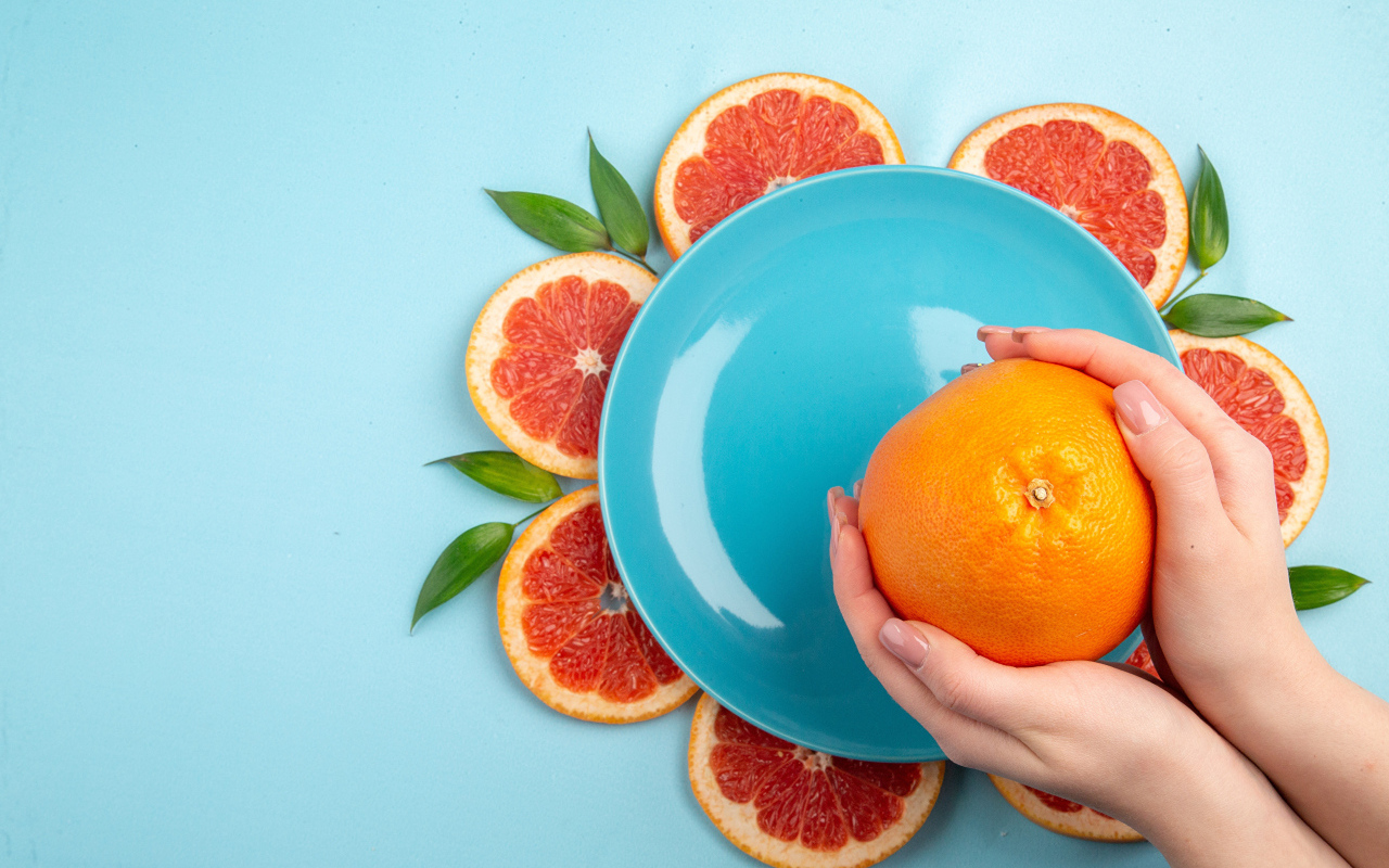 Апельсин в руках девушки на голубом фоне с тарелкой