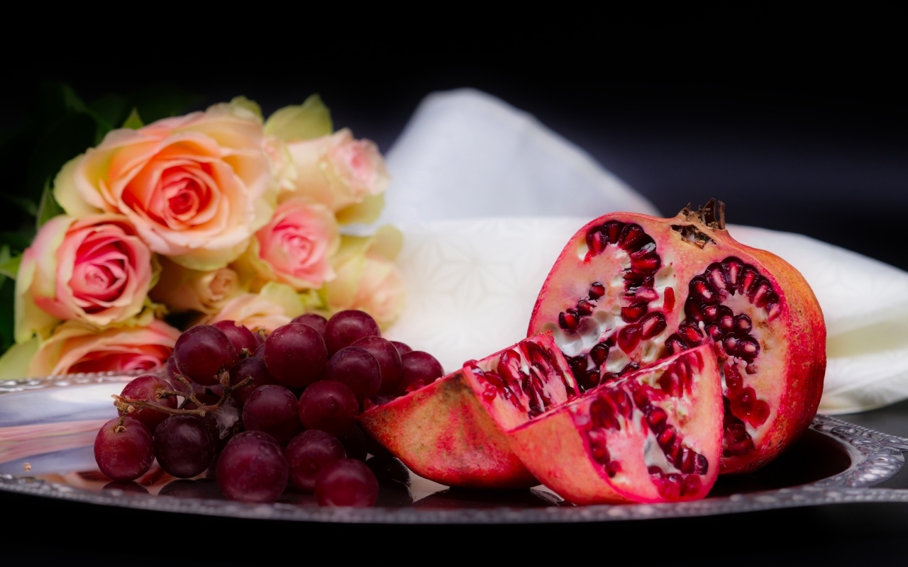 Гранат с виноградом на столе с букетом роз 