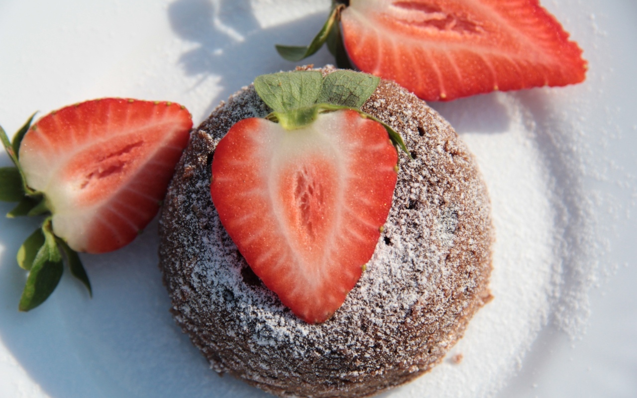 Пирожное на  тарелке с клубникой и сахарной пудрой