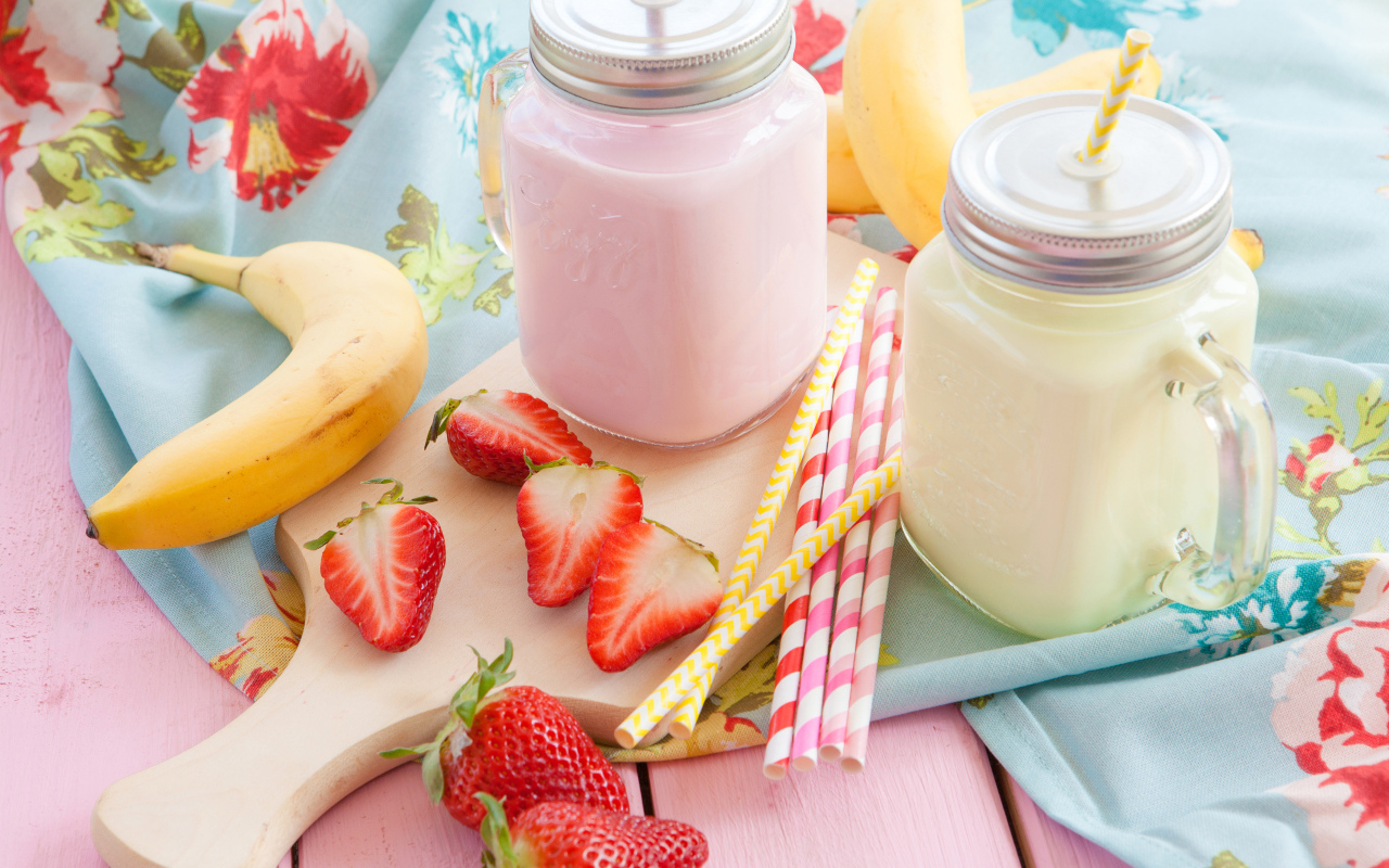 Две банки смузи на столе с бананом и ягодами клубники