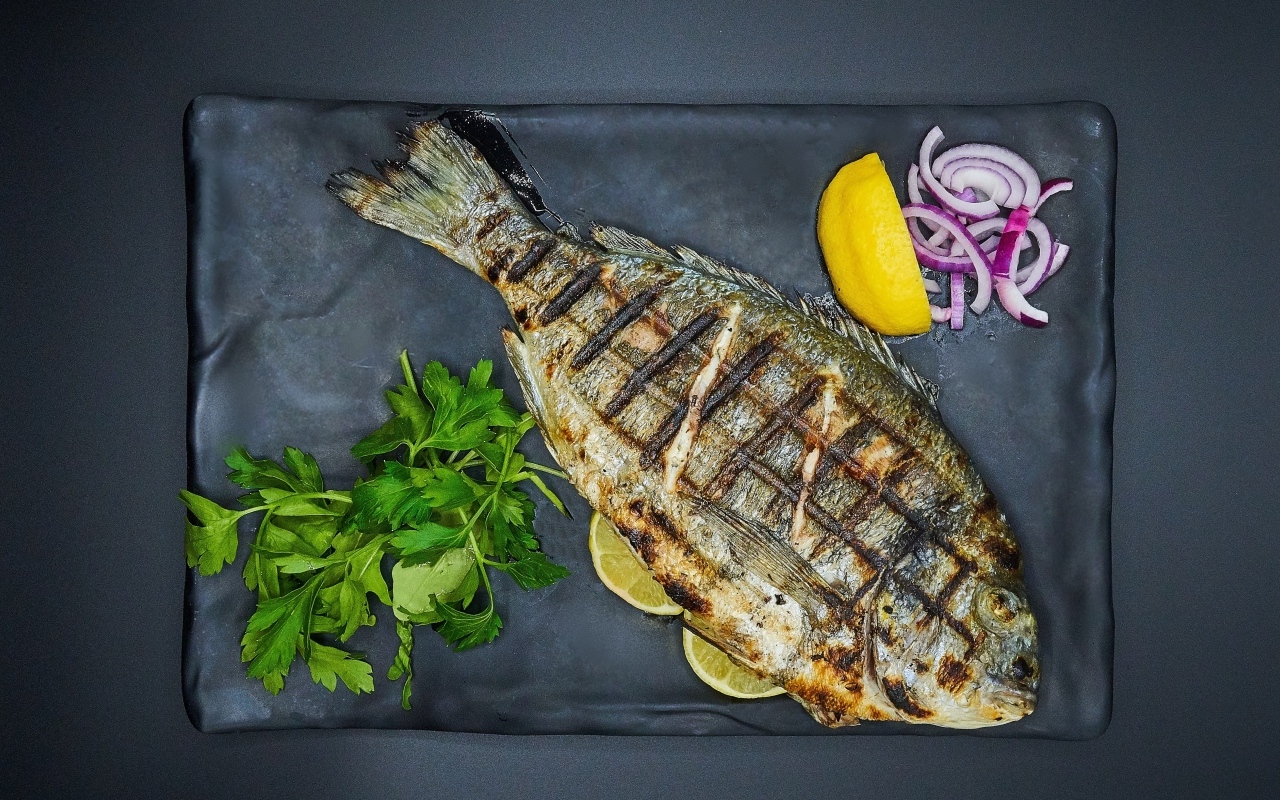 Жареная рыба с лимоном, луком и петрушкой на тарелке