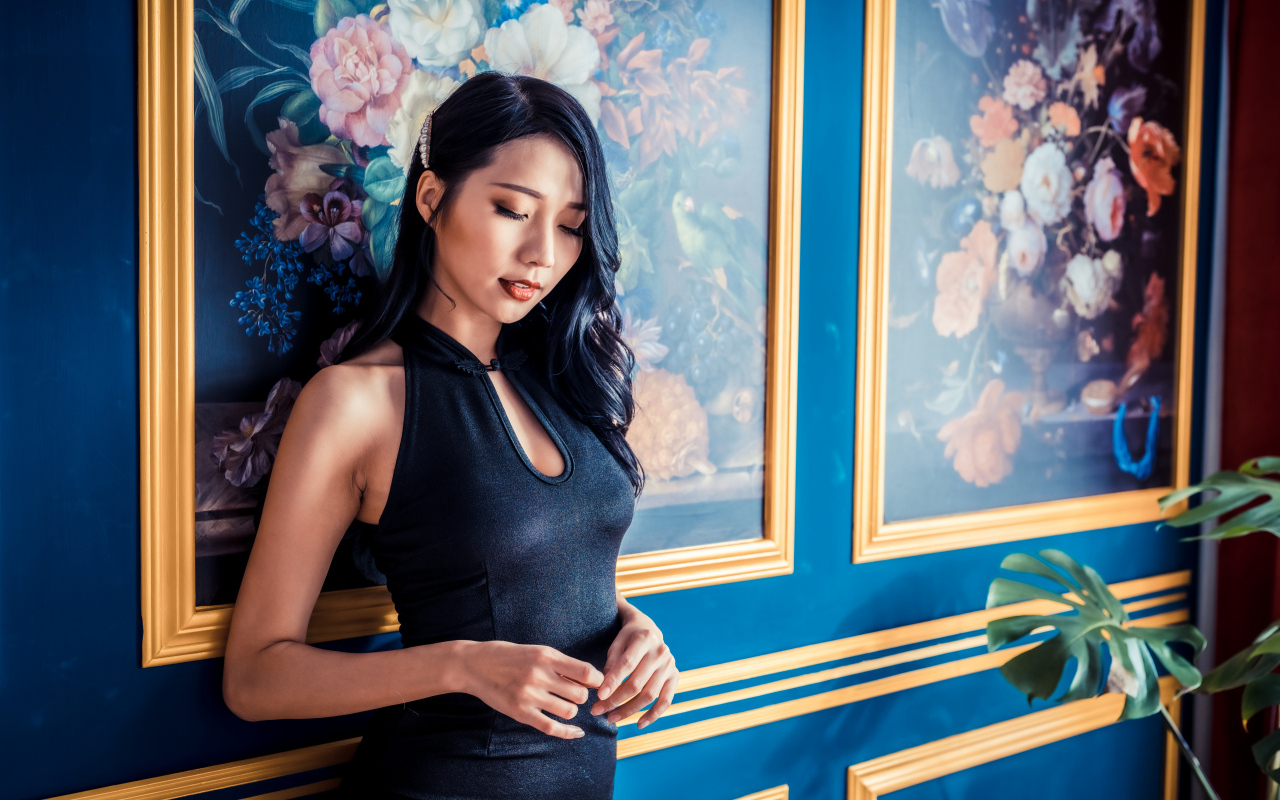 Красивая девушка азиатка в черном платье стоит у картины 