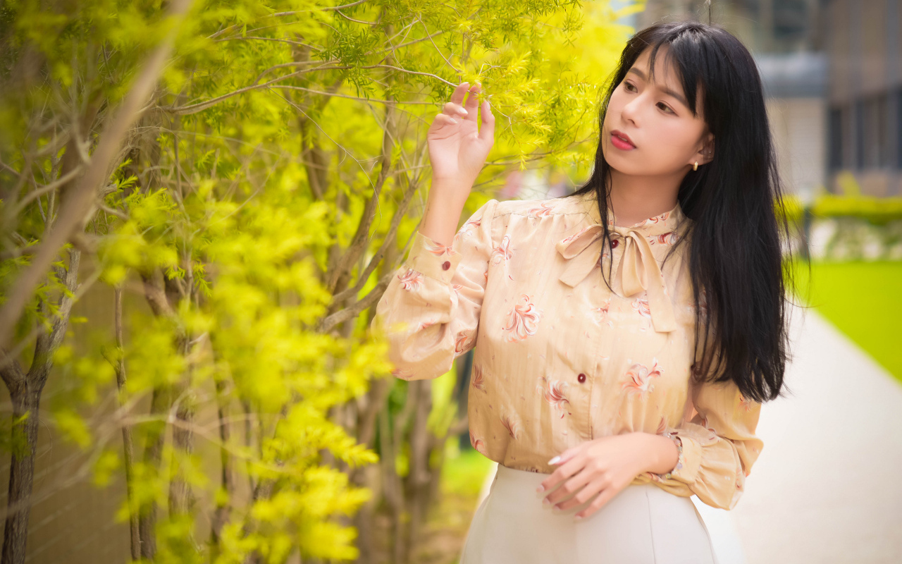 Молодая девушка азиатка стоит у дерева с зелеными листьями