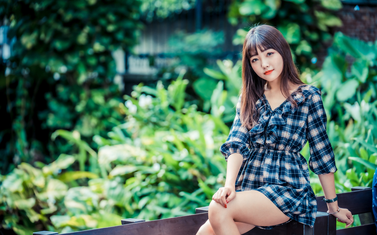 Молодая девушка в клетчатом платье сидит на заборе