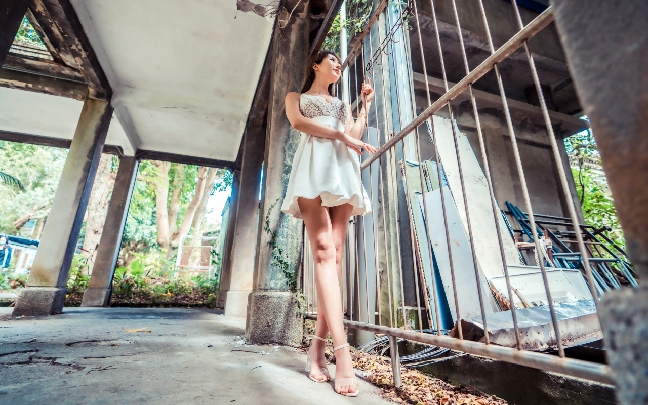 Девушка азиатка в платье стоит у решетки 