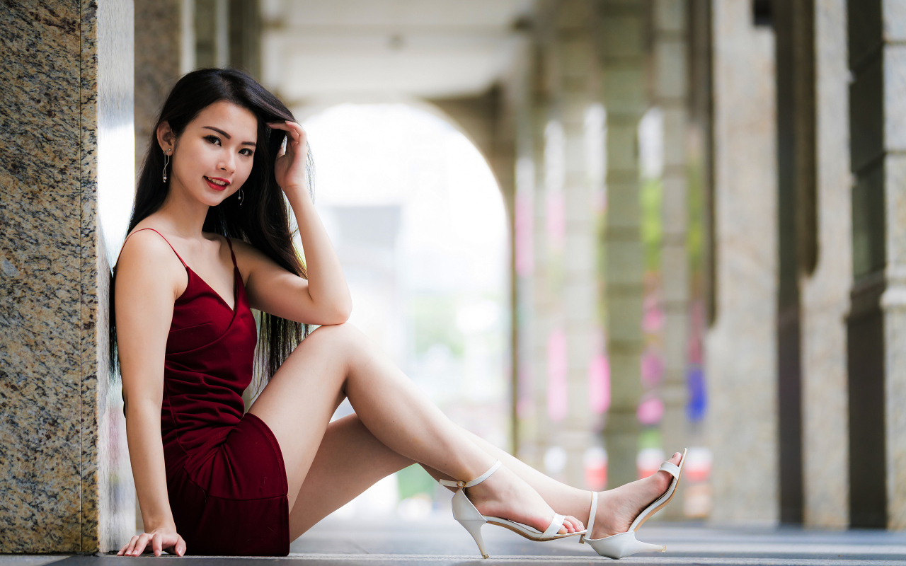 Азиатка в красном платье сидит у стены 