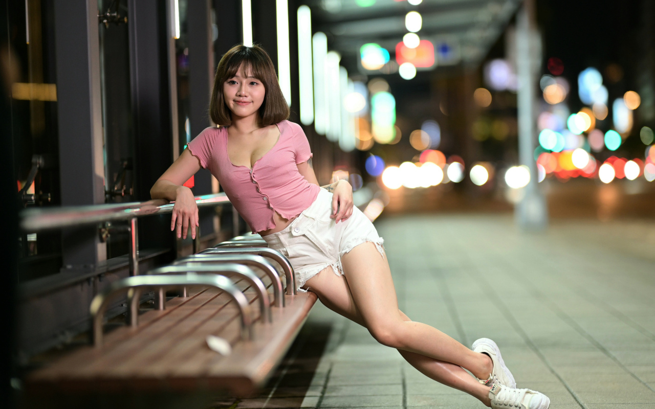 Азиатка в коротких белых шортах сидит на остановке