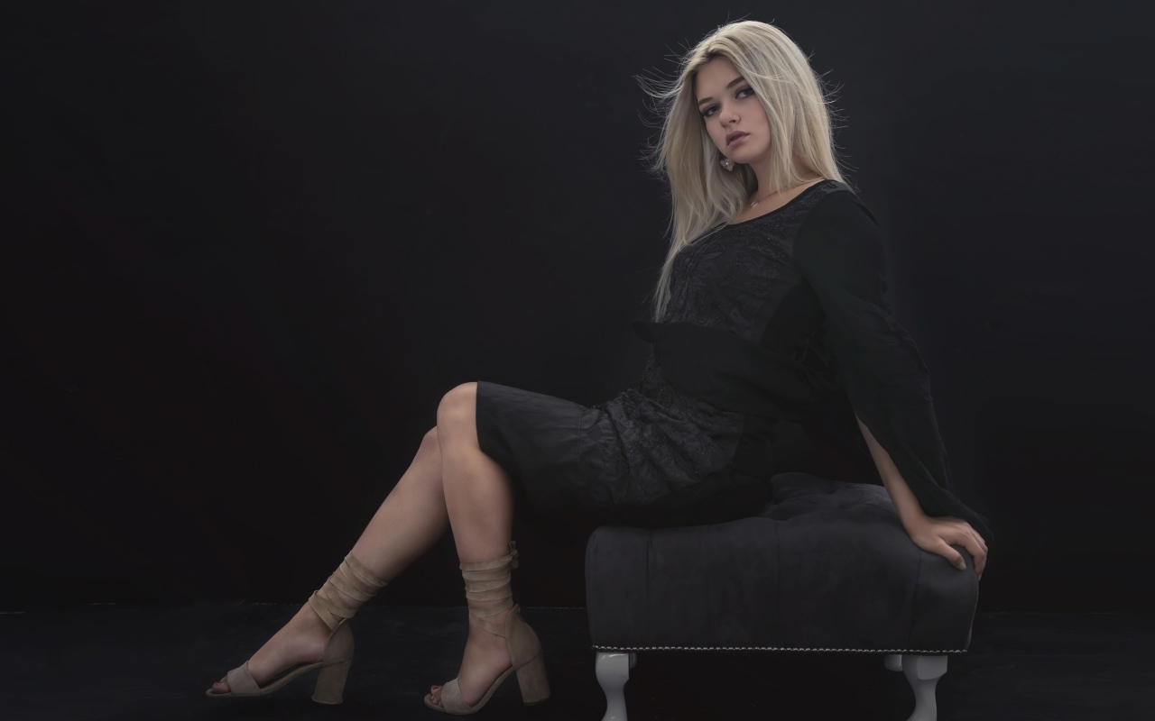 Красивая девушка в черном платье сидит на кресле