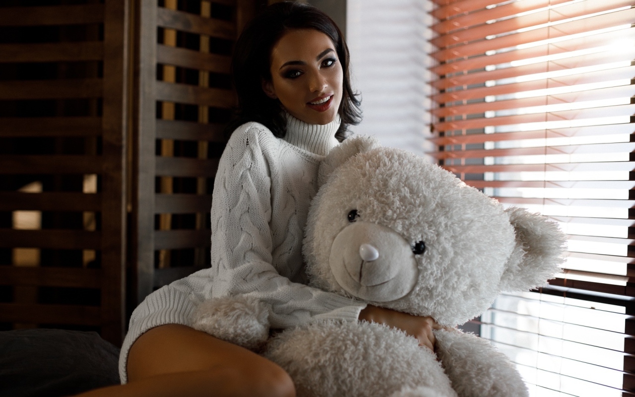 Красивая девушка в свитере с медведем у окна