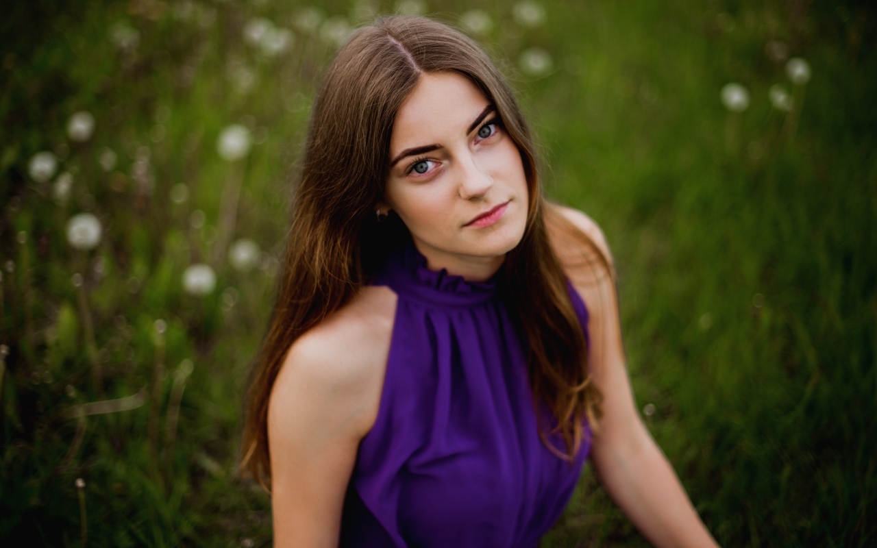 Милая девушка в фиолетовом платье сидит на траве
