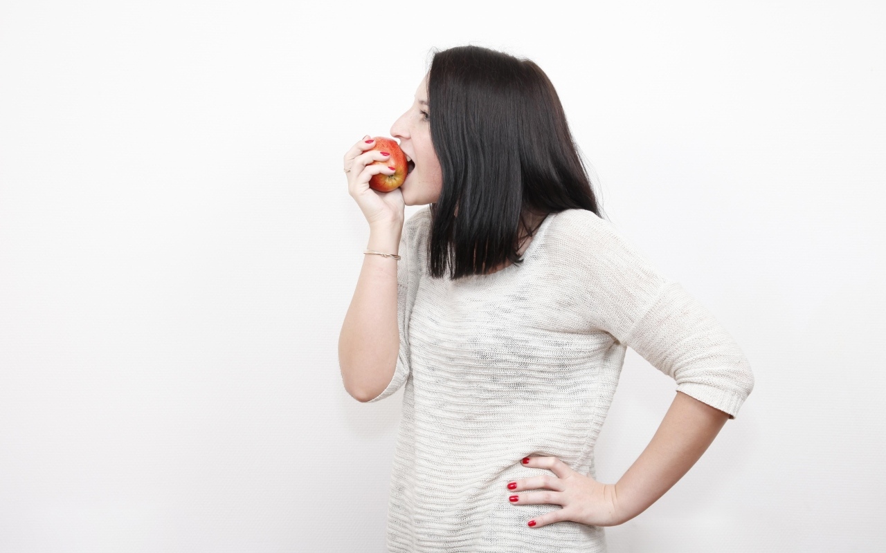 Девушка кусает красное яблоко 