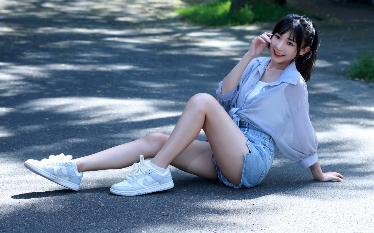 Улыбающаяся девушка азиатка в кедах сидит на дороге